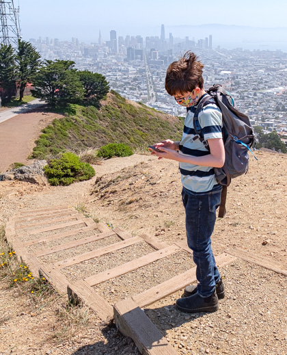 Photo of a boy looking at his phone. in the background is the city of San Francisco.